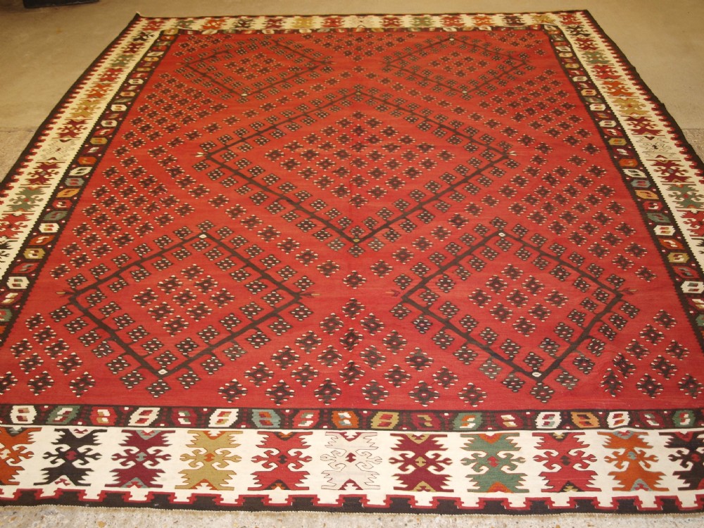 A large red wool Sharkoy flatweave kilim carpet featuring central geometric diamond patterns and a multi-coloured woven border.