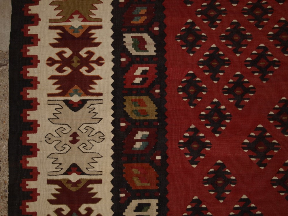 A large red wool Sharkoy flatweave kilim carpet featuring central geometric diamond patterns and a multi-coloured woven border. View IV