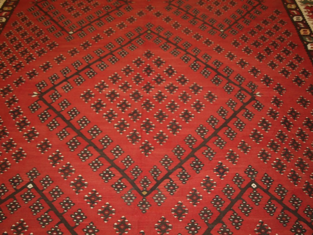 A large red wool Sharkoy flatweave kilim carpet featuring central geometric diamond patterns and a multi-coloured woven border. View V
