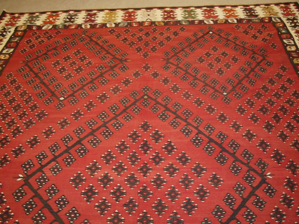 A large red wool Sharkoy flatweave kilim carpet featuring central geometric diamond patterns and a multi-coloured woven border. View VI