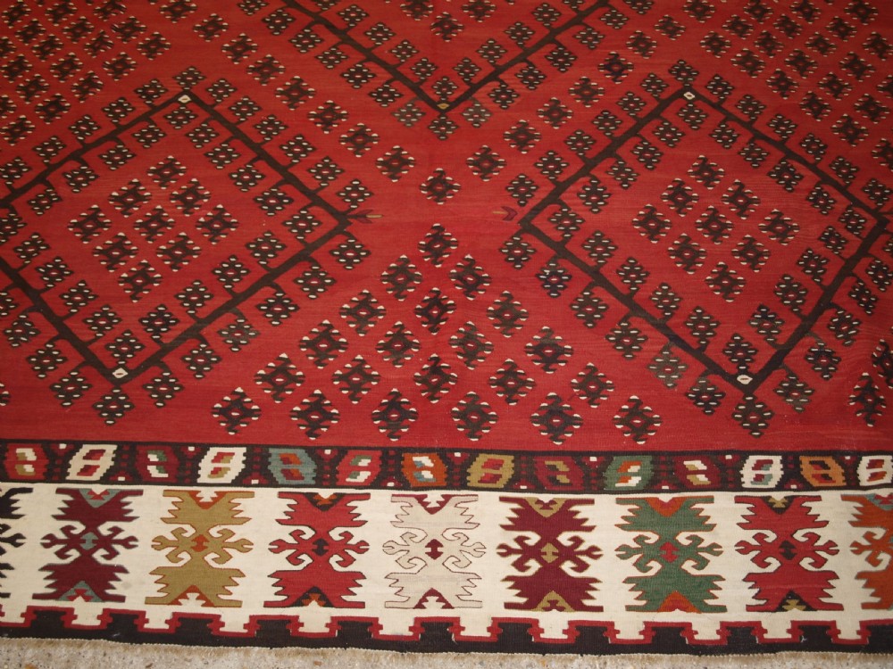 A large red wool Sharkoy flatweave kilim carpet featuring central geometric diamond patterns and a multi-coloured woven border. View VII