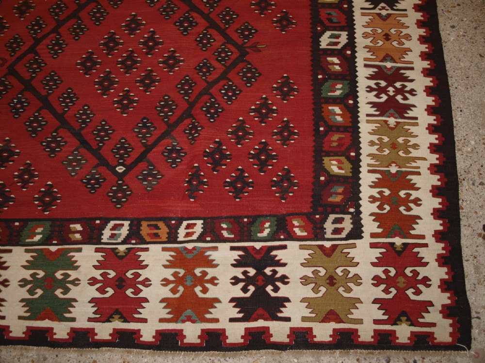 A large red wool Sharkoy flatweave kilim carpet featuring central geometric diamond patterns and a multi-coloured woven border. View VIII