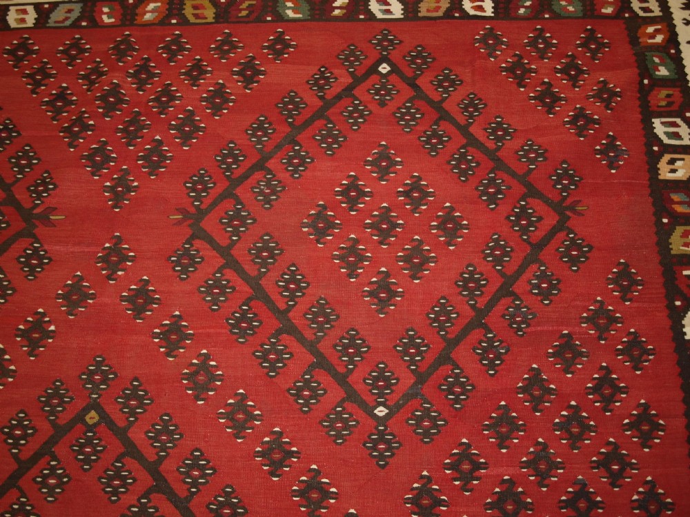 A large red wool Sharkoy flatweave kilim carpet featuring central geometric diamond patterns and a multi-coloured woven border. View IX