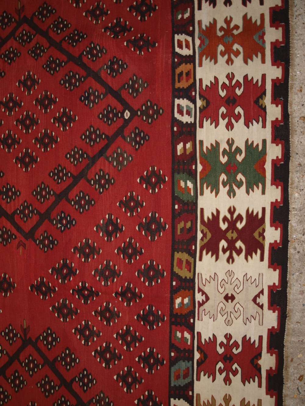 A large red wool Sharkoy flatweave kilim carpet featuring central geometric diamond patterns and a multi-coloured woven border. View X