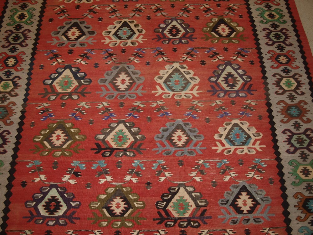 A handwoven flatweave kilim rug featuring a terracotta red central field with repeating multi-coloured geometric motifs and a decorative outer border. View VIII