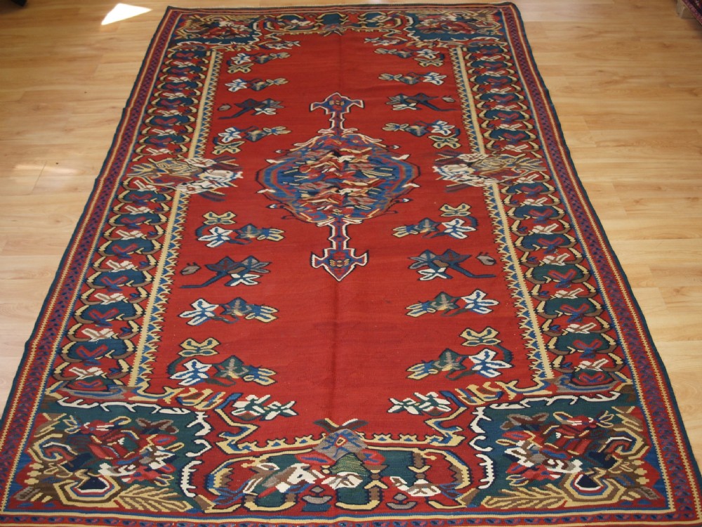 An antique Persian Bijar flatweave kilim rug featuring a deep red central field with a central geometric medallion and floral motifs surrounded by decorative borders.