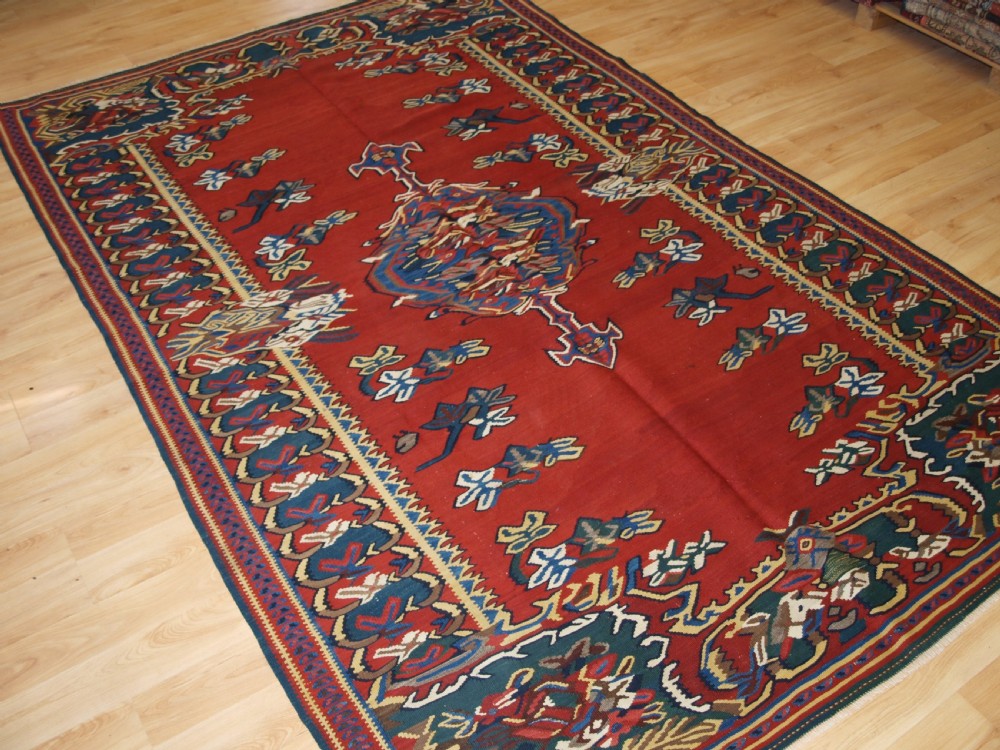 An antique Persian Bijar flatweave kilim rug featuring a deep red central field with a central geometric medallion and floral motifs surrounded by decorative borders. View III