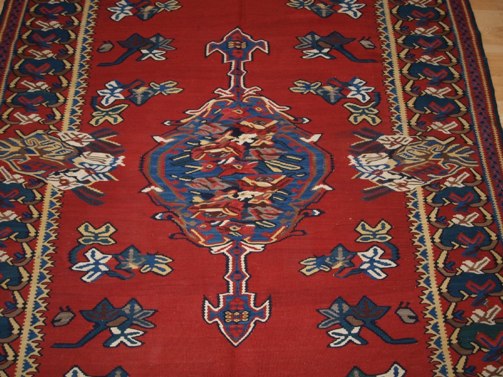 An antique Persian Bijar flatweave kilim rug featuring a deep red central field with a central geometric medallion and floral motifs surrounded by decorative borders. View IV