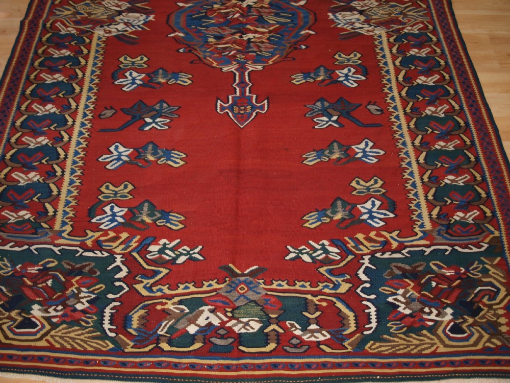 An antique Persian Bijar flatweave kilim rug featuring a deep red central field with a central geometric medallion and floral motifs surrounded by decorative borders. View V