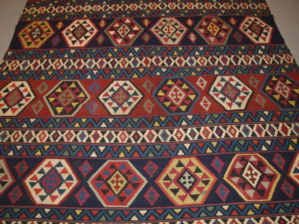 A large flat-woven antique Caucasian Shirvan kilim rug featuring horizontal bands of geometric diamond motifs in red, navy blue, green, and yellow. View III