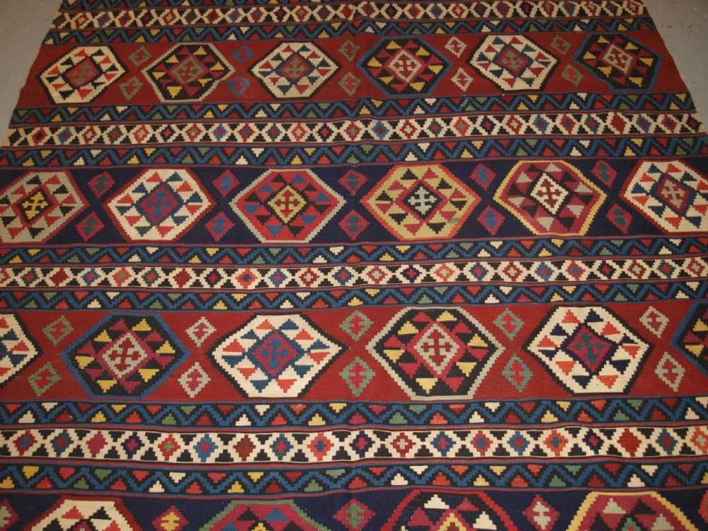 A large flat-woven antique Caucasian Shirvan kilim rug featuring horizontal bands of geometric diamond motifs in red, navy blue, green, and yellow. View IV