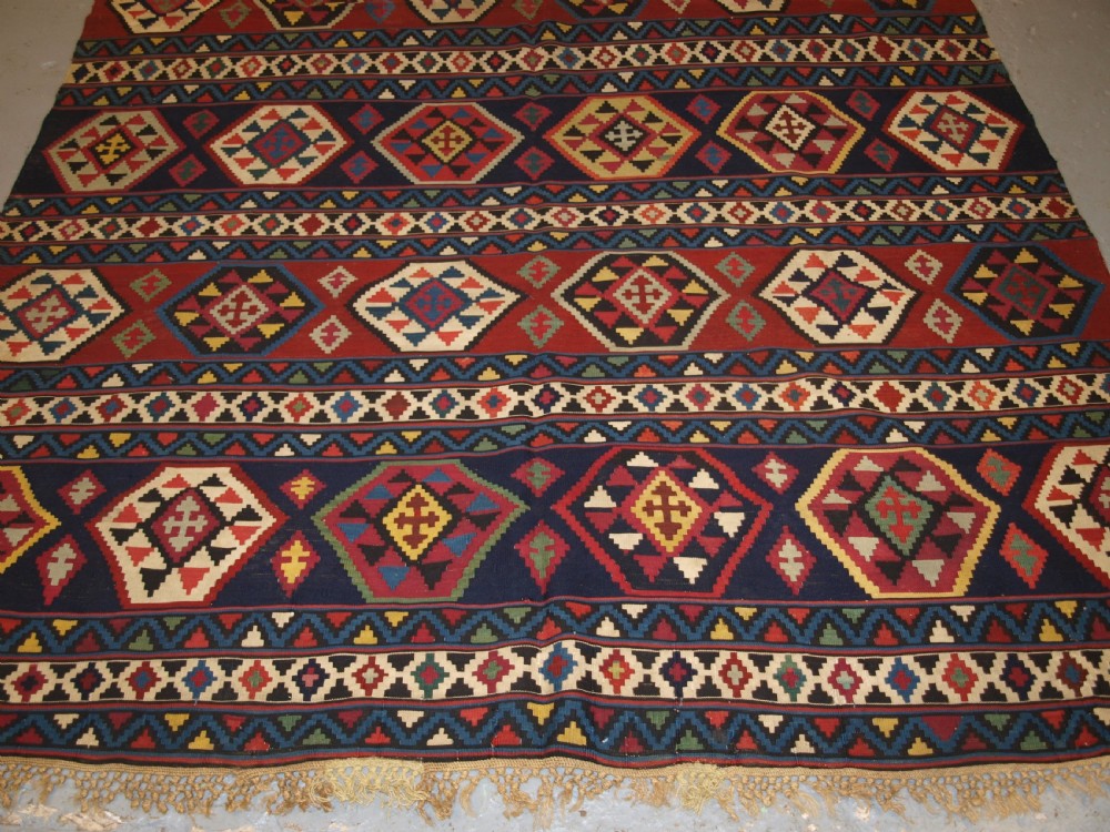 A large flat-woven antique Caucasian Shirvan kilim rug featuring horizontal bands of geometric diamond motifs in red, navy blue, green, and yellow. View V