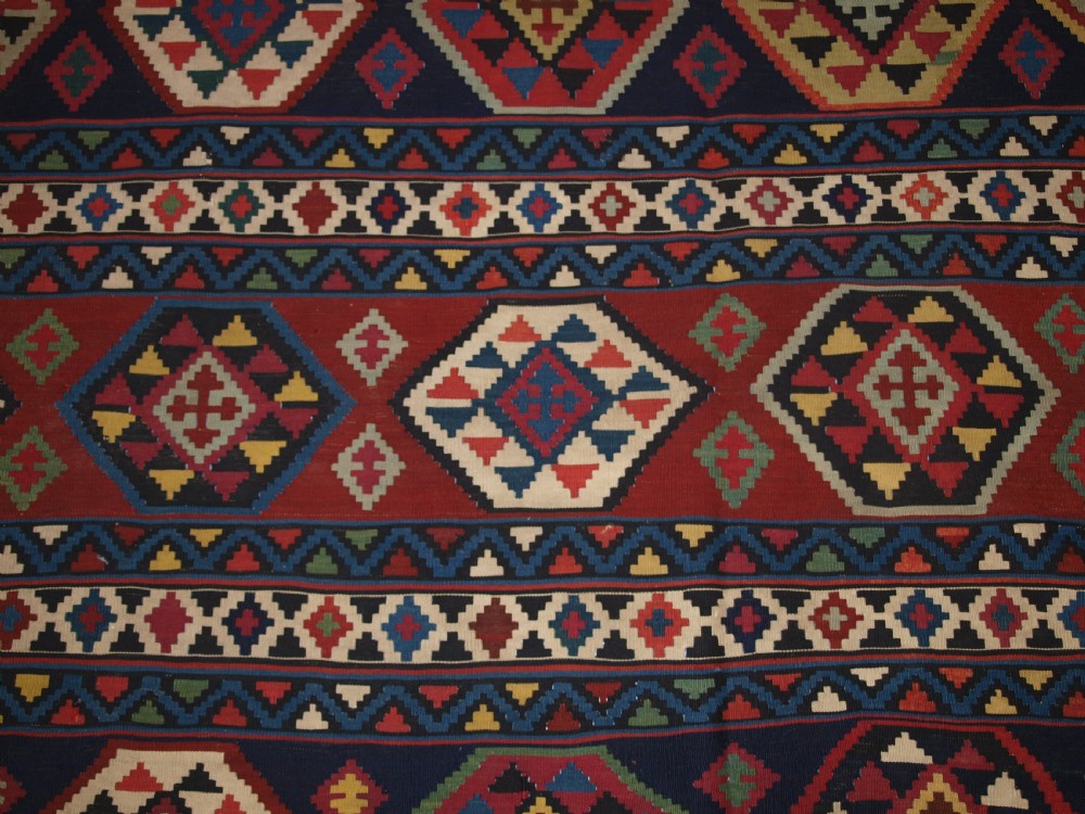 A large flat-woven antique Caucasian Shirvan kilim rug featuring horizontal bands of geometric diamond motifs in red, navy blue, green, and yellow. View VIII