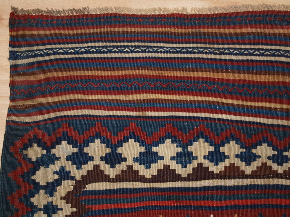 An antique handwoven Persian Varamin kilim rug featuring horizontal bands of blue, terracotta, and cream with repeating geometric diamond motifs. View III
