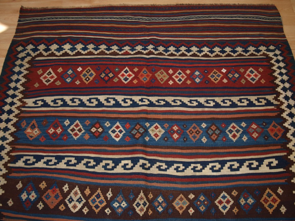 An antique handwoven Persian Varamin kilim rug featuring horizontal bands of blue, terracotta, and cream with repeating geometric diamond motifs. View IV