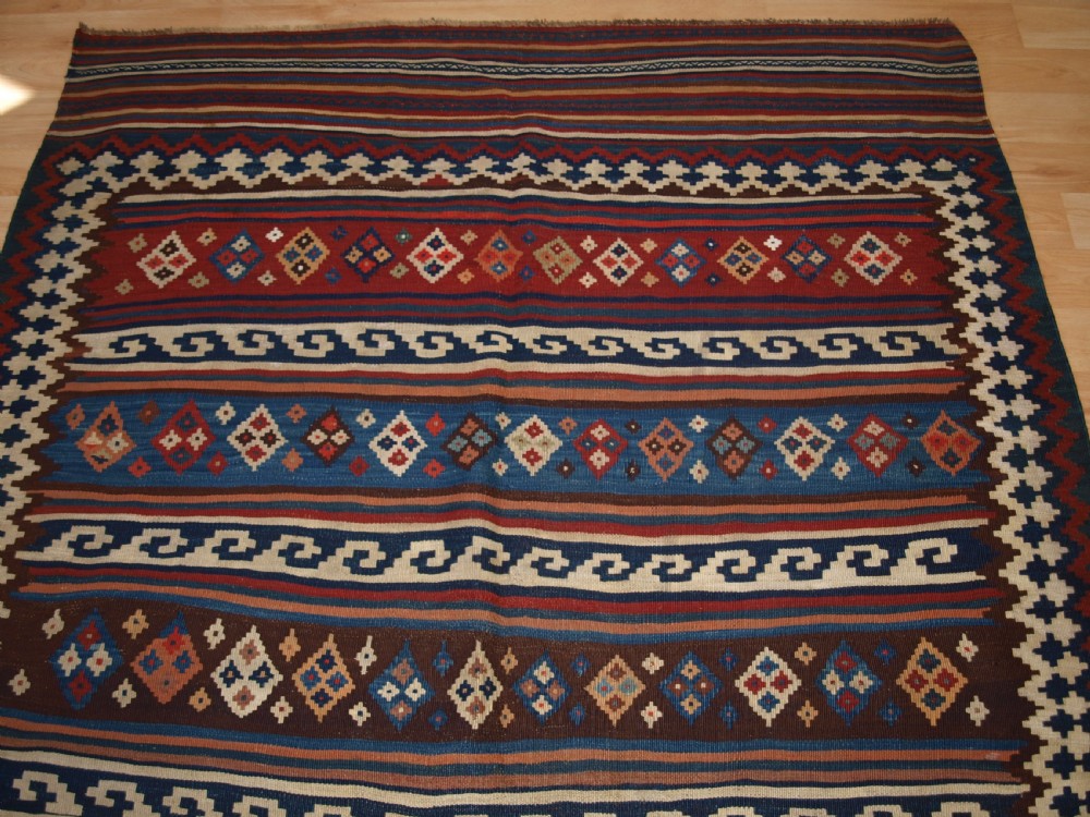 An antique handwoven Persian Varamin kilim rug featuring horizontal bands of blue, terracotta, and cream with repeating geometric diamond motifs. View V