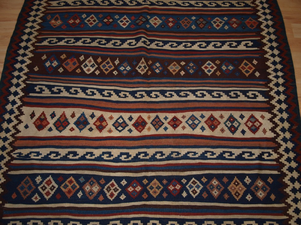An antique handwoven Persian Varamin kilim rug featuring horizontal bands of blue, terracotta, and cream with repeating geometric diamond motifs. View VI