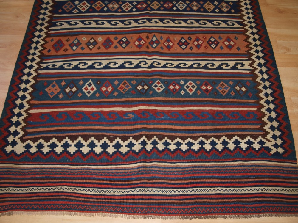 An antique handwoven Persian Varamin kilim rug featuring horizontal bands of blue, terracotta, and cream with repeating geometric diamond motifs. View VII