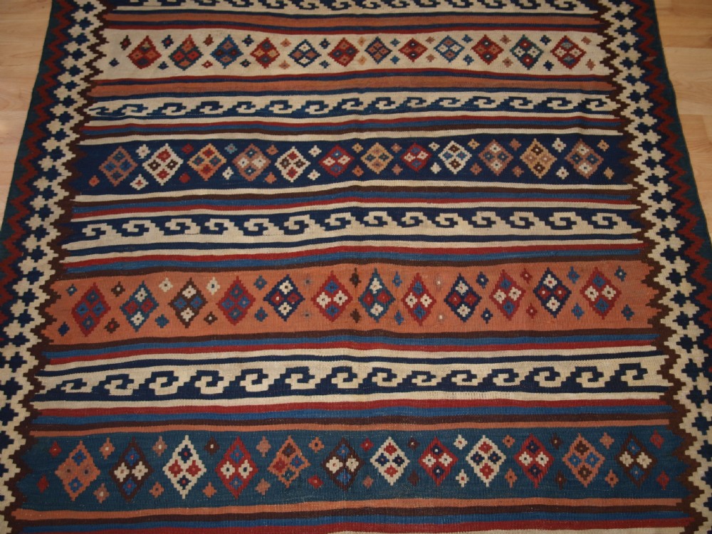 An antique handwoven Persian Varamin kilim rug featuring horizontal bands of blue, terracotta, and cream with repeating geometric diamond motifs. View VIII