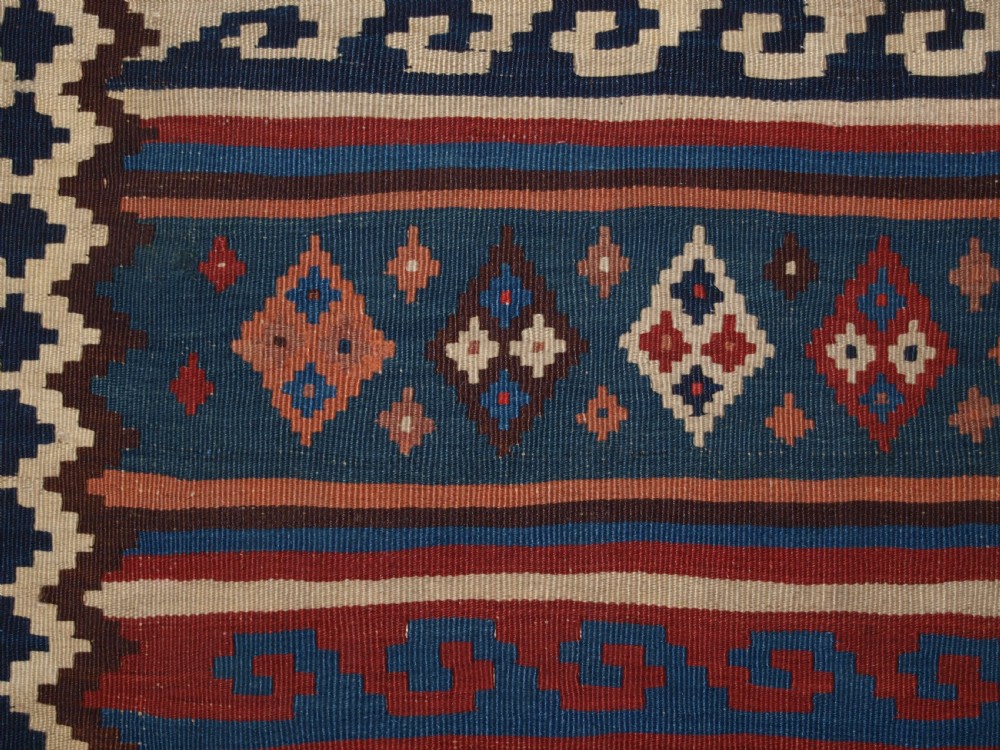 An antique handwoven Persian Varamin kilim rug featuring horizontal bands of blue, terracotta, and cream with repeating geometric diamond motifs. View IX