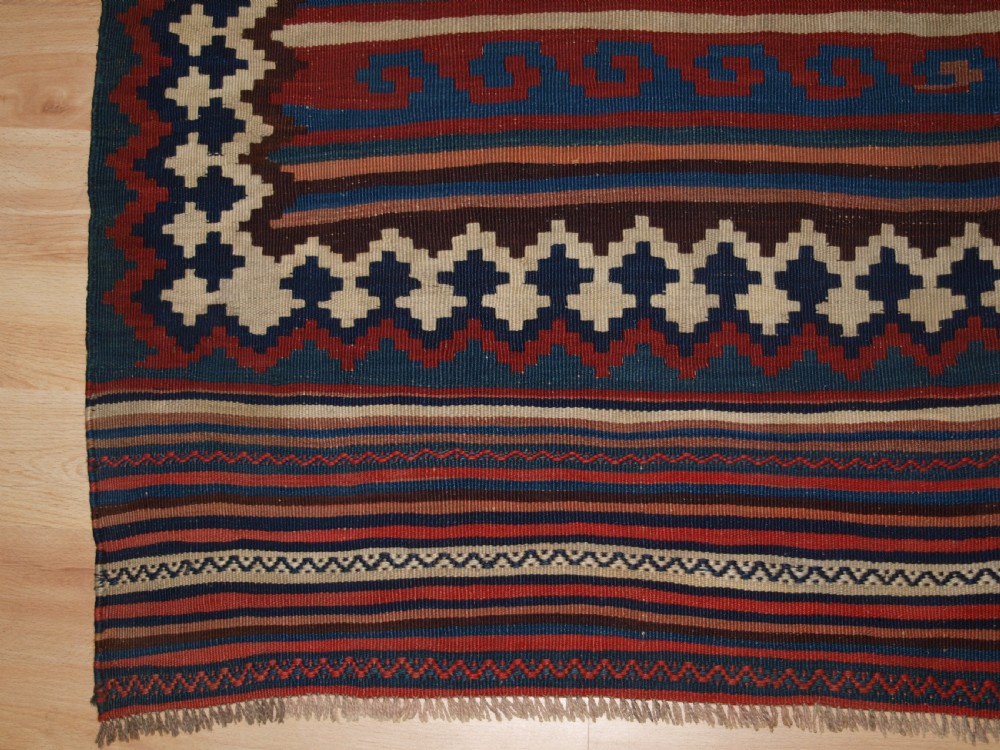 An antique handwoven Persian Varamin kilim rug featuring horizontal bands of blue, terracotta, and cream with repeating geometric diamond motifs. View X
