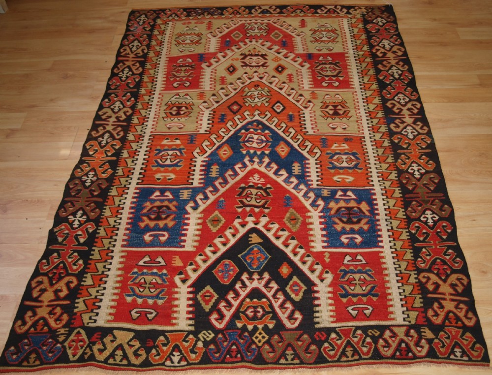 An antique Turkish Konya flatweave prayer kilim featuring a stepped mihrab pattern in red, blue, terracotta, and beige wool.