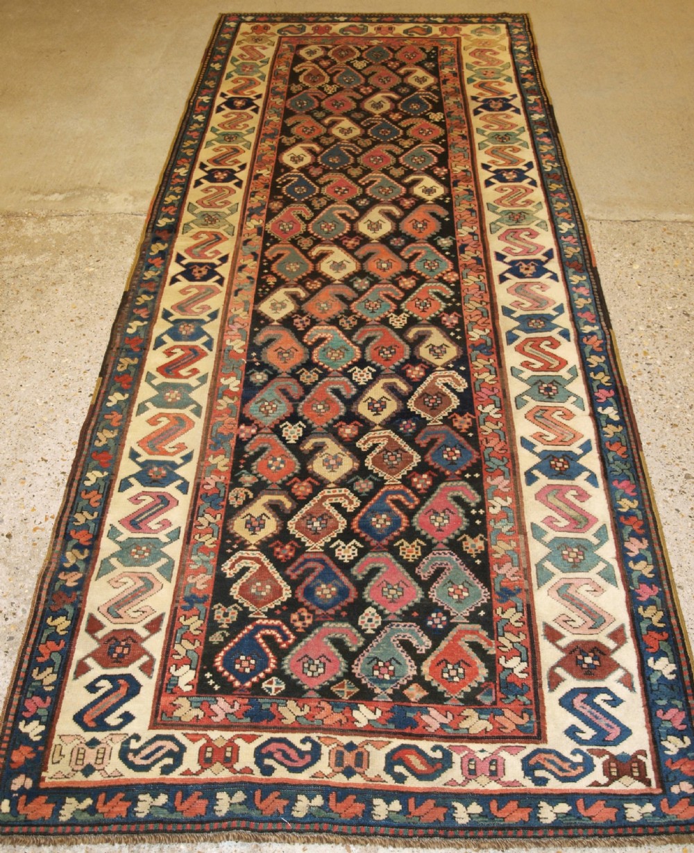 An antique 19th-century Caucasian Karabagh hallway runner carpet featuring colourful repeated boteh motifs across a dark central field framed by ivory geometric borders.