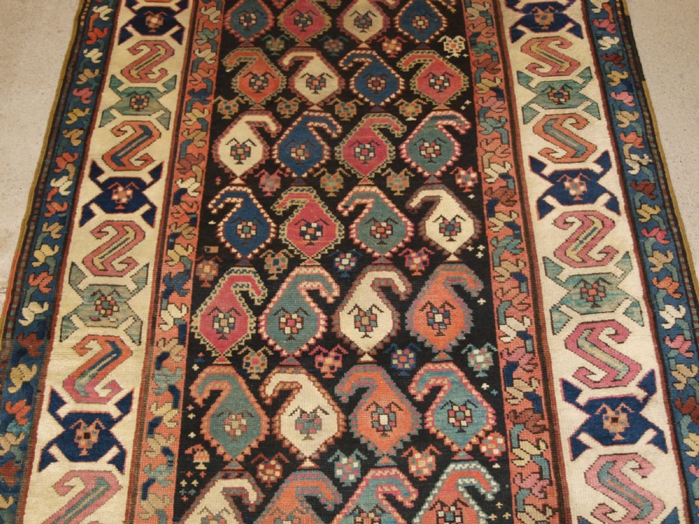 An antique 19th-century Caucasian Karabagh hallway runner carpet featuring colourful repeated boteh motifs across a dark central field framed by ivory geometric borders. View V
