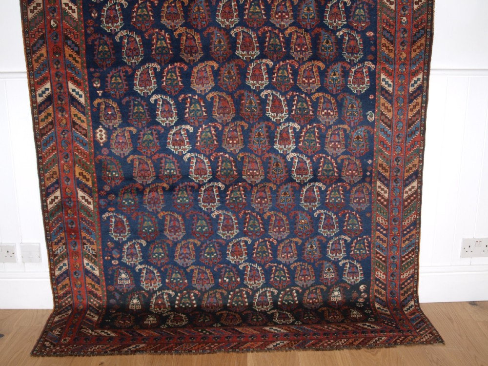 An antique Afshar long rug featuring a dark navy blue central field densely filled with repeating multi-coloured boteh motifs, bordered by geometric stripes. View IV