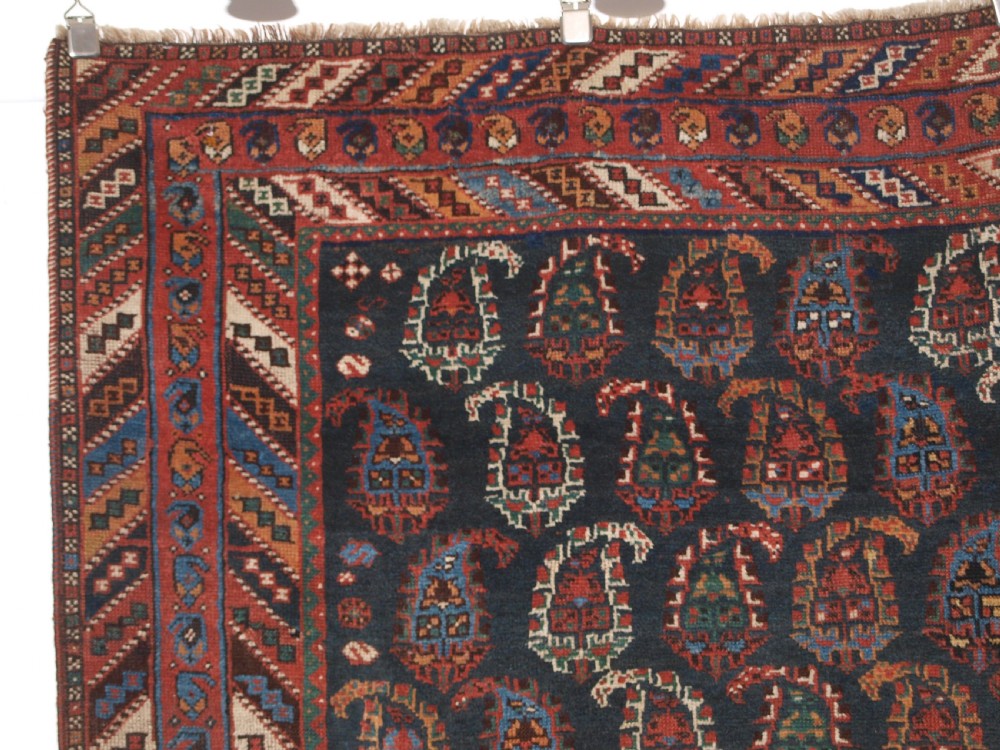 An antique Afshar long rug featuring a dark navy blue central field densely filled with repeating multi-coloured boteh motifs, bordered by geometric stripes. View V