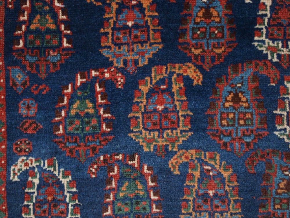 An antique Afshar long rug featuring a dark navy blue central field densely filled with repeating multi-coloured boteh motifs, bordered by geometric stripes. View VII