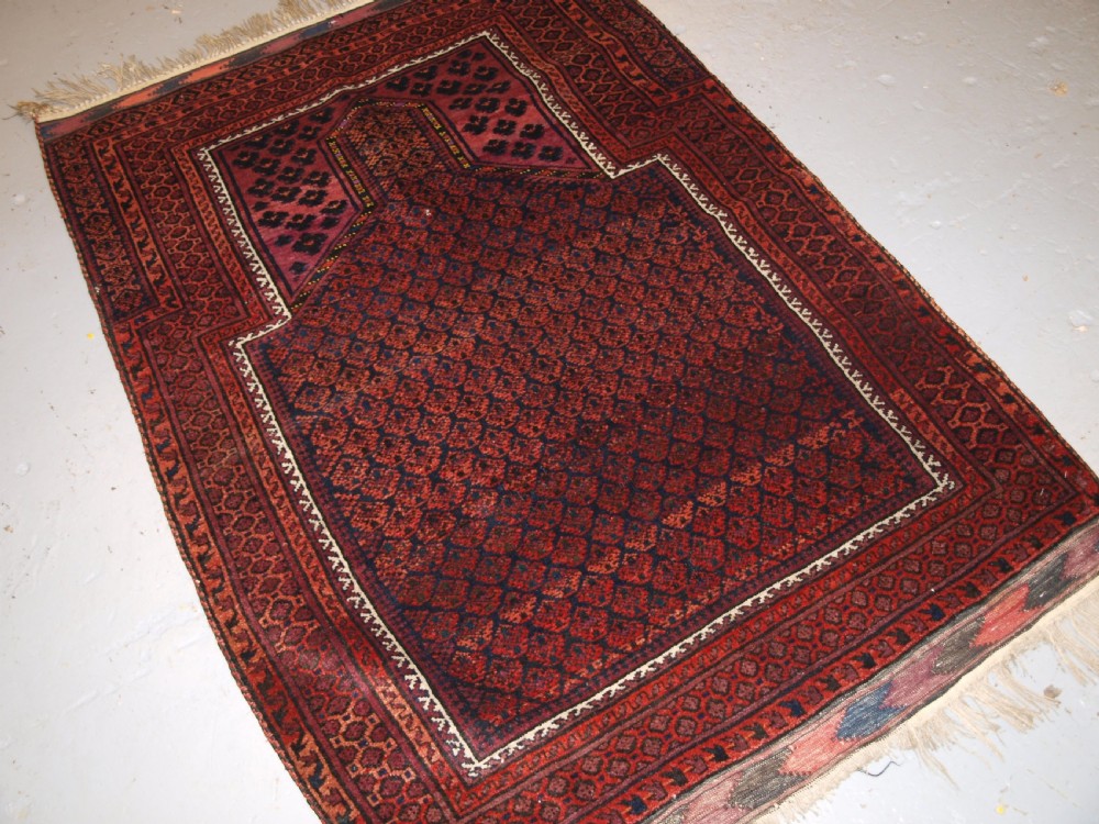 An antique hand-knotted Baluch prayer rug featuring a pointed mihrab arch motif, geometric lattice patterning, and a dark red and indigo colour palette. View II