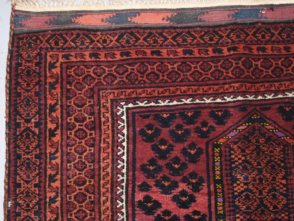 An antique hand-knotted Baluch prayer rug featuring a pointed mihrab arch motif, geometric lattice patterning, and a dark red and indigo colour palette. View III