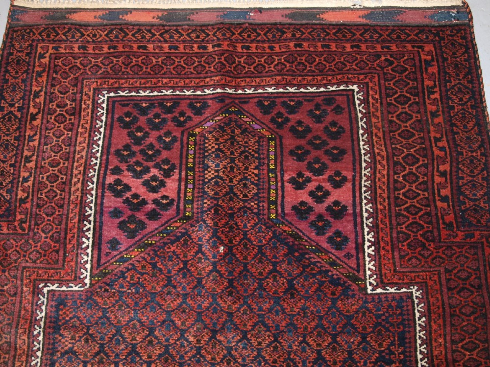 An antique hand-knotted Baluch prayer rug featuring a pointed mihrab arch motif, geometric lattice patterning, and a dark red and indigo colour palette. View IV