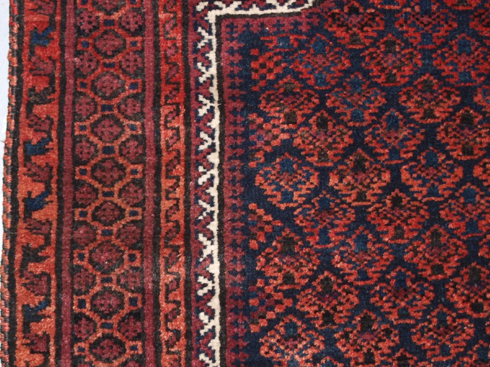 An antique hand-knotted Baluch prayer rug featuring a pointed mihrab arch motif, geometric lattice patterning, and a dark red and indigo colour palette. View V