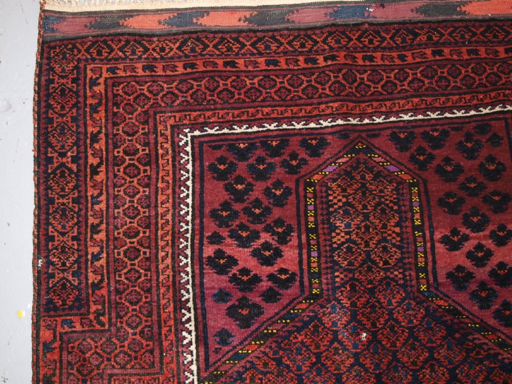 An antique hand-knotted Baluch prayer rug featuring a pointed mihrab arch motif, geometric lattice patterning, and a dark red and indigo colour palette. View VII