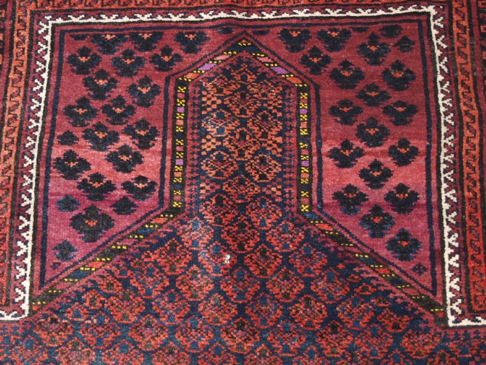 An antique hand-knotted Baluch prayer rug featuring a pointed mihrab arch motif, geometric lattice patterning, and a dark red and indigo colour palette. View X