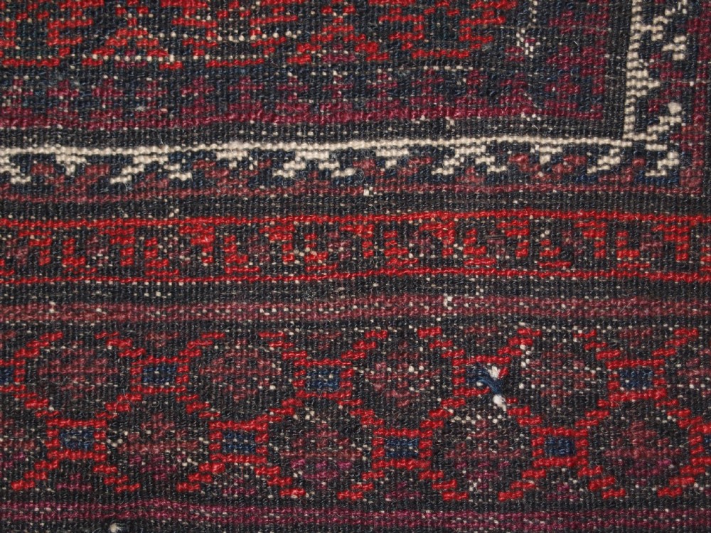 An antique hand-knotted Baluch prayer rug featuring a pointed mihrab arch motif, geometric lattice patterning, and a dark red and indigo colour palette. View XI