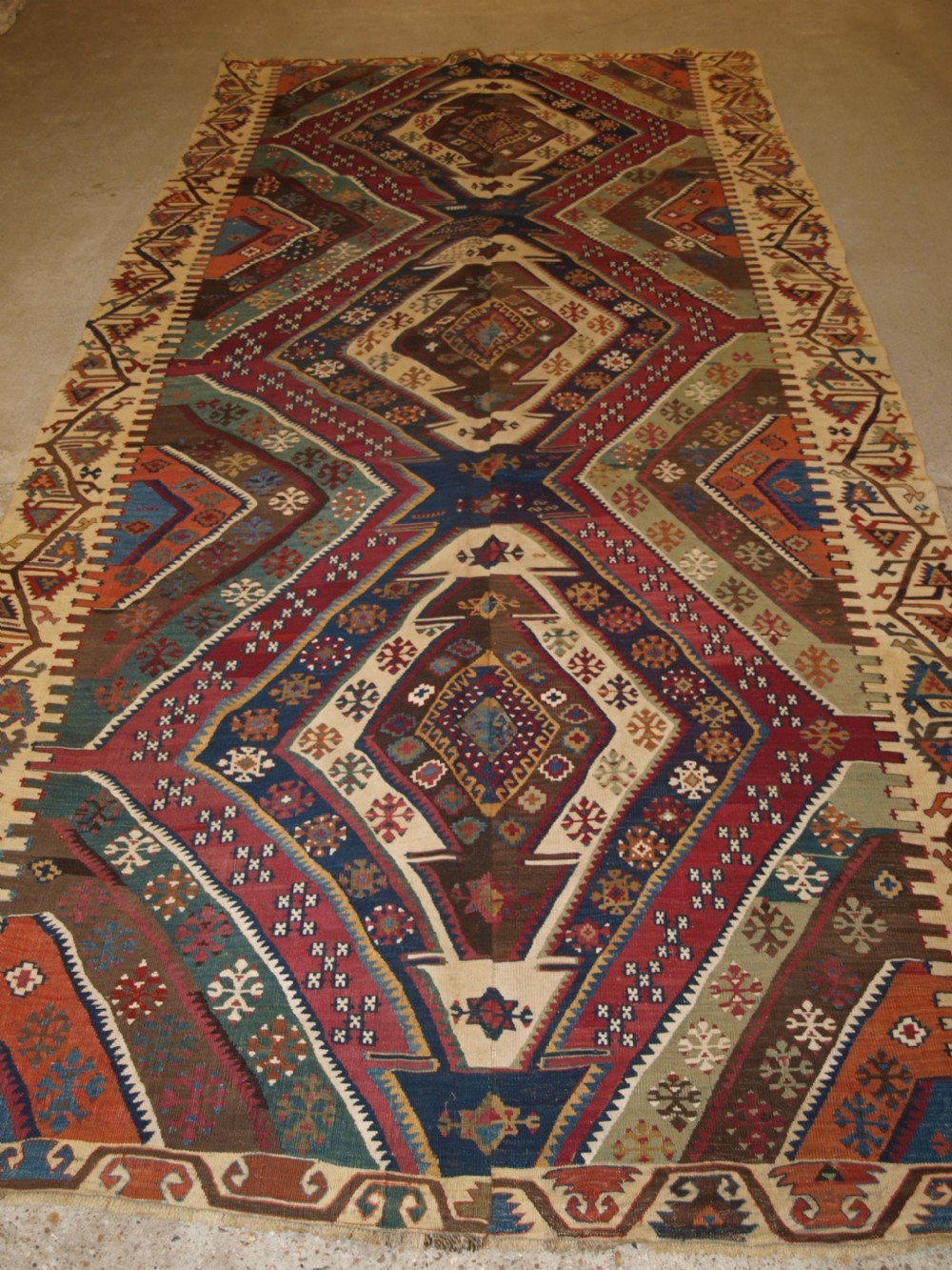 A late 19th-century handwoven Turkish Malatya kilim rug featuring complex geometric diamond medallions in terracotta red, navy blue, green, and cream wool.