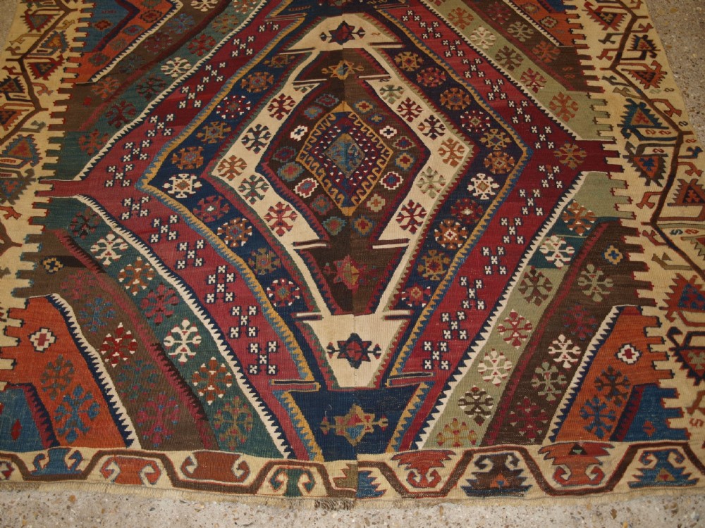A late 19th-century handwoven Turkish Malatya kilim rug featuring complex geometric diamond medallions in terracotta red, navy blue, green, and cream wool. View X