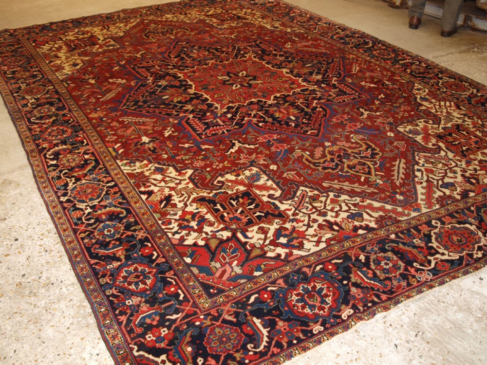 A large hand-knotted Persian Heriz carpet featuring a prominent geometric central medallion in dark navy and red, framed by cream spandrels and a wide dark border.