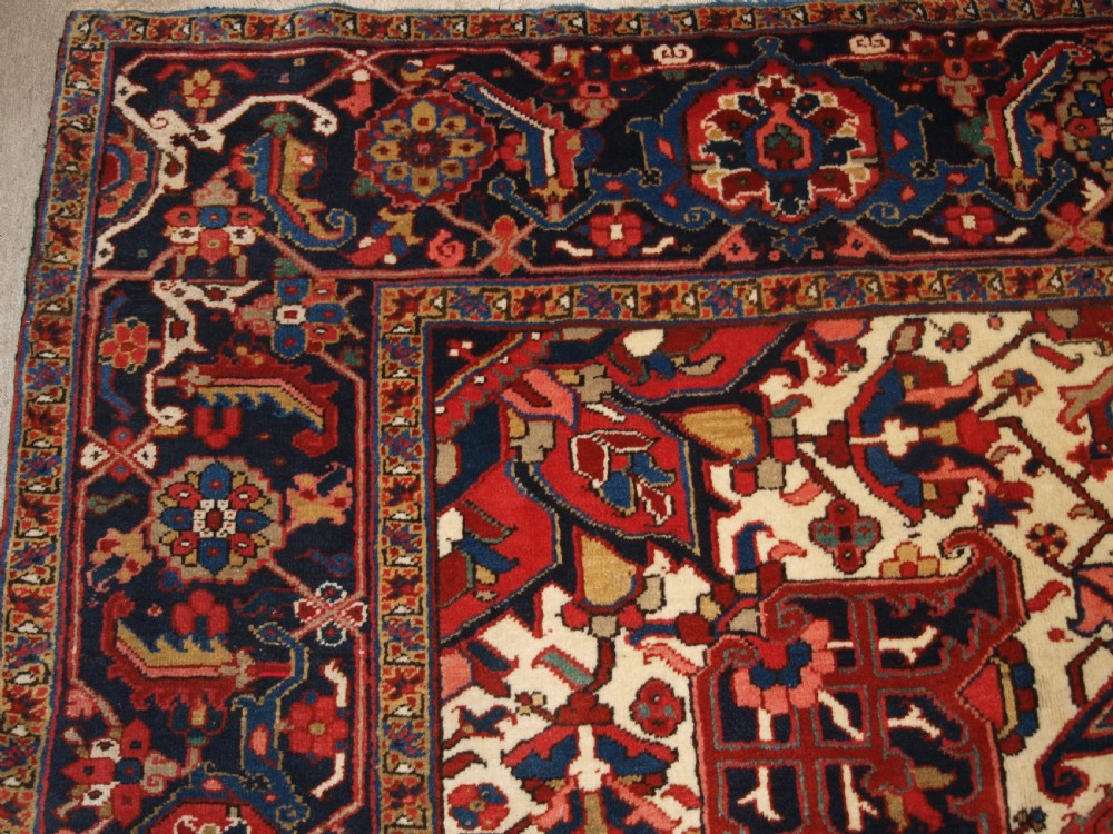 A large hand-knotted Persian Heriz carpet featuring a prominent geometric central medallion in dark navy and red, framed by cream spandrels and a wide dark border. View II