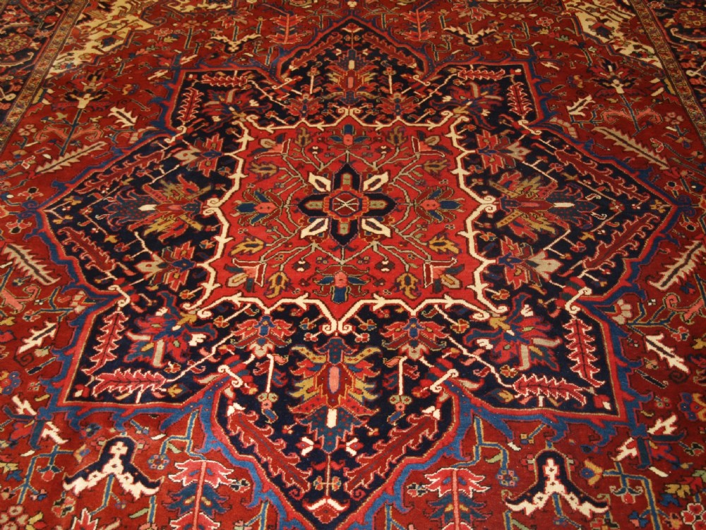 A large hand-knotted Persian Heriz carpet featuring a prominent geometric central medallion in dark navy and red, framed by cream spandrels and a wide dark border. View V