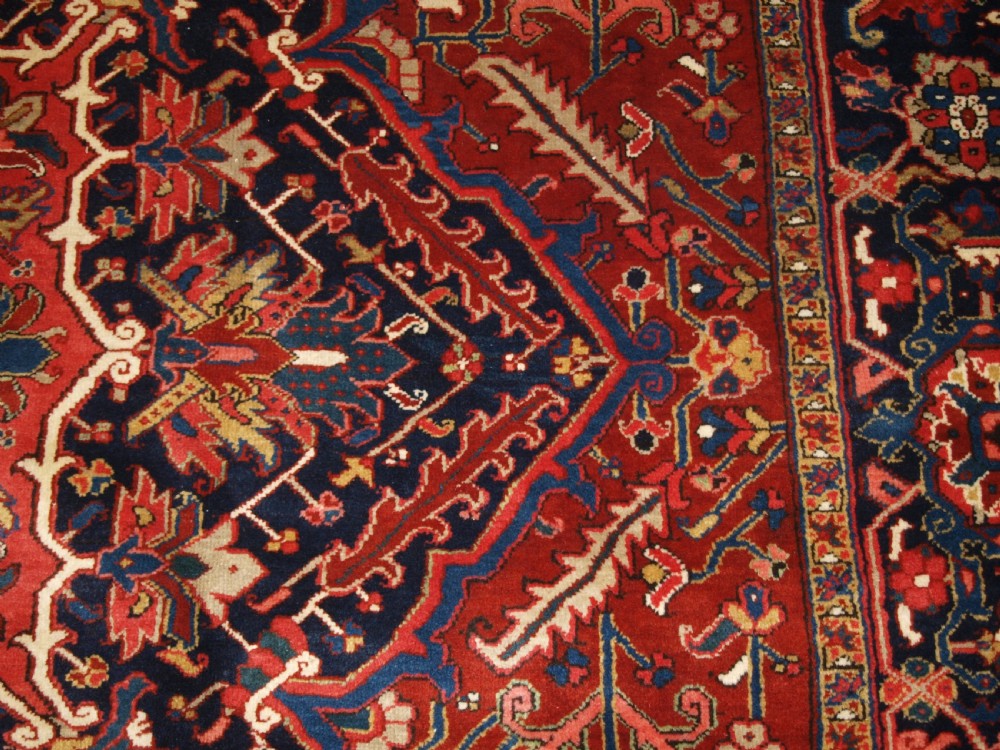 A large hand-knotted Persian Heriz carpet featuring a prominent geometric central medallion in dark navy and red, framed by cream spandrels and a wide dark border. View IX