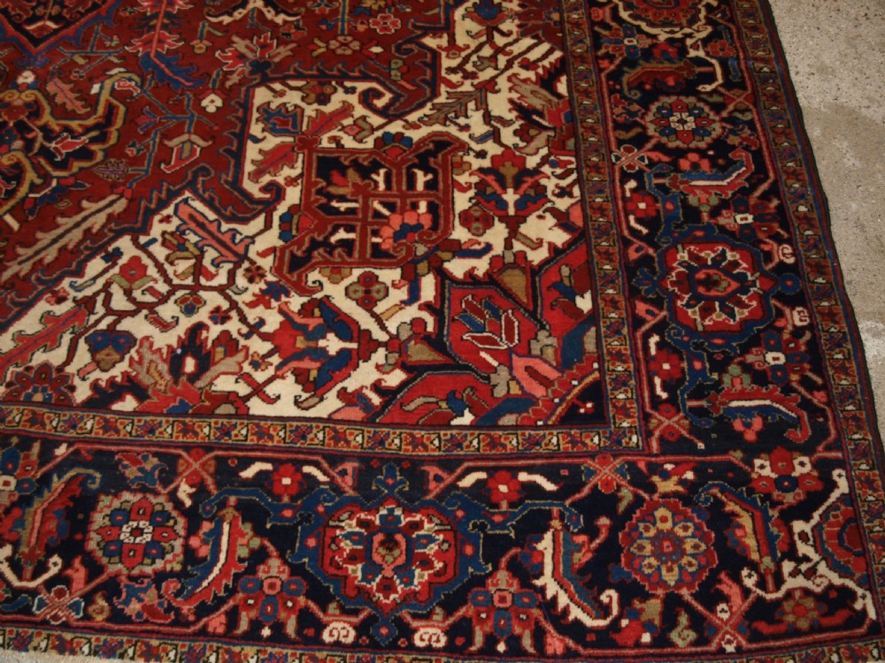 A large hand-knotted Persian Heriz carpet featuring a prominent geometric central medallion in dark navy and red, framed by cream spandrels and a wide dark border. View X