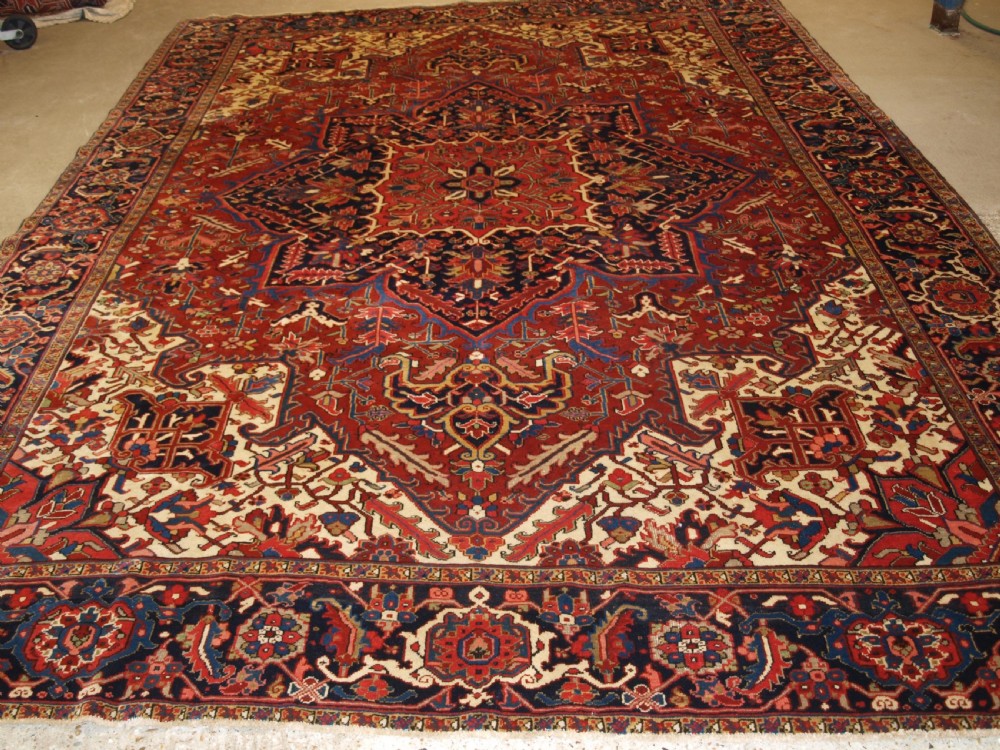 A large hand-knotted Persian Heriz carpet featuring a prominent geometric central medallion in dark navy and red, framed by cream spandrels and a wide dark border. View XI