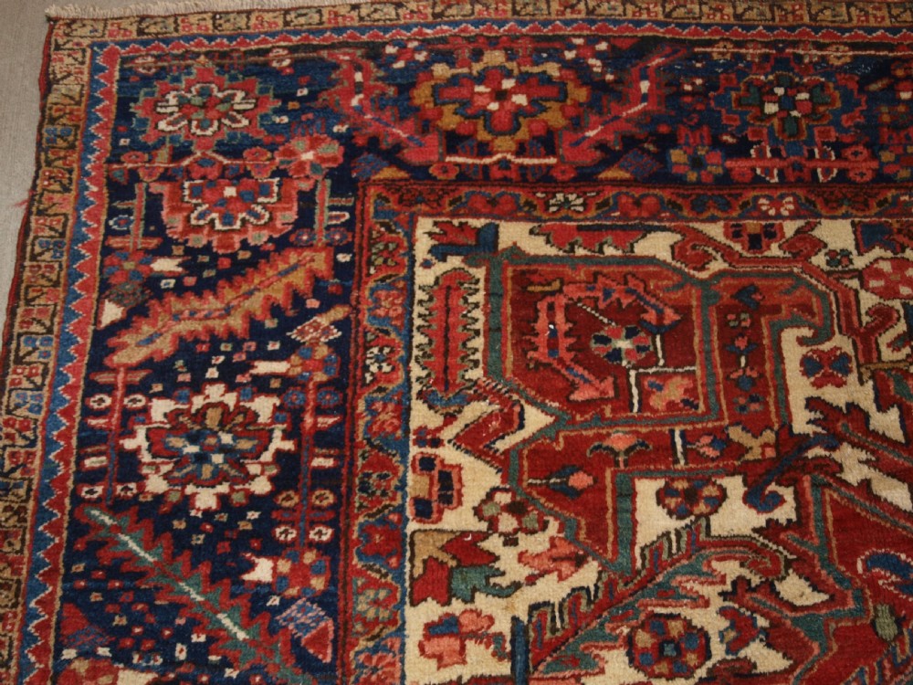 An antique Persian Heriz wool carpet featuring a bold red field with a central geometric medallion, ivory spandrels, and navy blue floral borders. View II