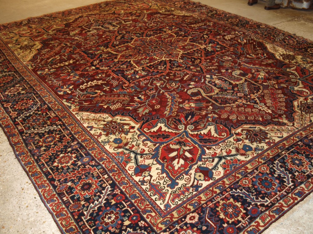 A large hand-knotted Persian Heriz wool carpet featuring a bold central geometric medallion in rust red, dark indigo, and ivory tones.