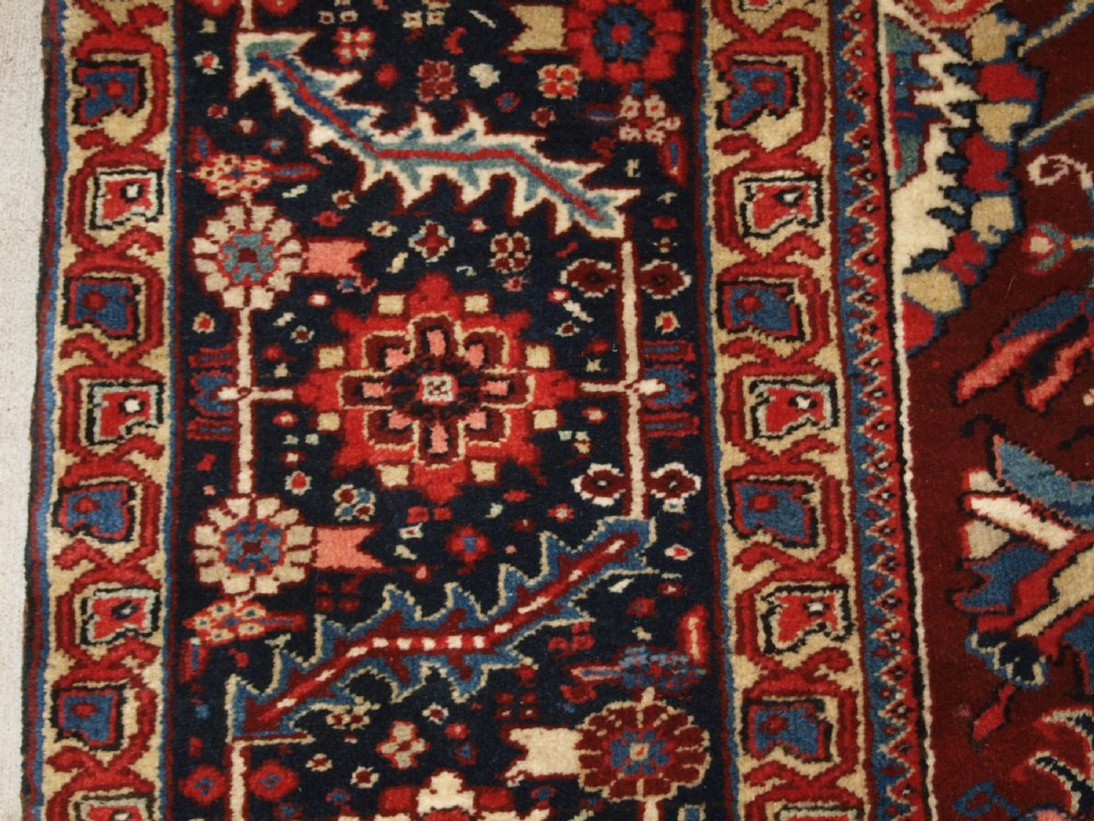 A large hand-knotted Persian Heriz wool carpet featuring a bold central geometric medallion in rust red, dark indigo, and ivory tones. View III