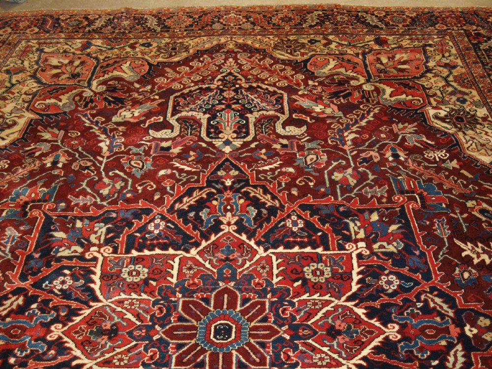A large hand-knotted Persian Heriz wool carpet featuring a bold central geometric medallion in rust red, dark indigo, and ivory tones. View IV